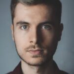 Close-up portrait of a young man with facial hair and a serious expression.